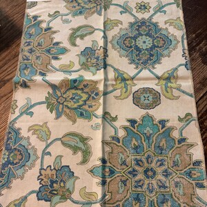 May include: A fabric swatch featuring a floral pattern in shades of blue, green, and tan on a cream background. The design includes large stylized flowers and geometric shapes. The label reads "Brooklyn Ocean".