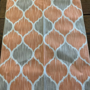 May include: A fabric swatch with a repeating geometric pattern in mango orange and gray. The pattern is a series of overlapping ovals with a textured, brushstroke effect. The fabric has a white background. The label reads "Temple Furniture".