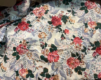 May include: A white fabric with a floral pattern. The flowers are pink, red, and yellow. The leaves are green. The fabric has a subtle sheen.