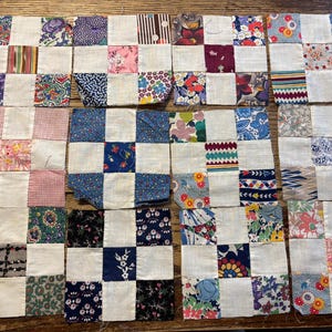 May include: A collection of small, square quilt blocks arranged in rows. Each block features a white square alternating with a patterned fabric square. The fabrics display floral, geometric, and abstract designs in various colors.