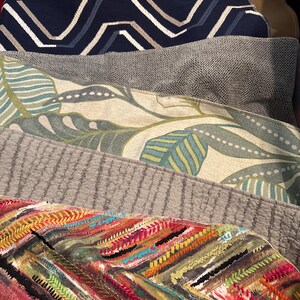 Peut inclure: Un ensemble d'échantillons de tissus colorés avec différents motifs, dont un motif géométrique bleu et blanc, un motif floral vert et blanc, un motif texturé gris et un motif rayé multicolore.