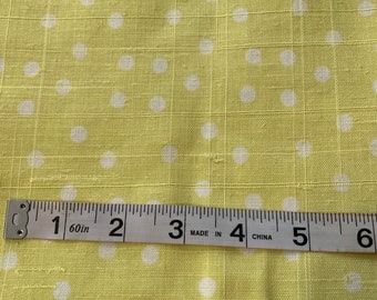 May include: A close-up of a yellow fabric with white polka dots. A measuring tape is placed on top of the fabric, showing measurements from 1 to 6 inches.