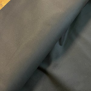 May include: Black fabric with a smooth, slightly textured surface. The fabric is folded in half, showing the inside and outside of the material.