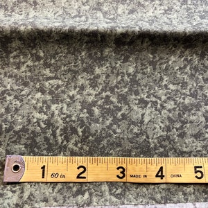 May include: Close-up of a green and gray fabric with a speckled pattern. A ruler is placed on the fabric, showing measurements in inches.