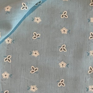 May include: A light blue fabric with a white floral pattern. The fabric has a subtle texture and a slightly sheer appearance.