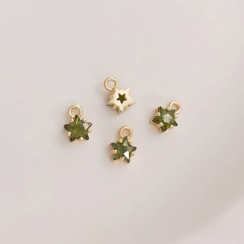 May include: Four gold star charms with green crystal accents. The charms have a loop at the top for attaching to jewelry.