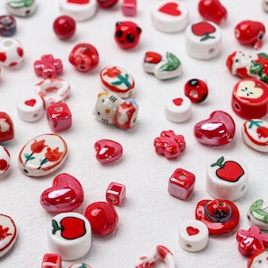 Peut inclure: Assortiment de perles en céramique rouge et blanche avec différents motifs, notamment des cœurs, des fleurs, des pommes et un personnage Hello Kitty.