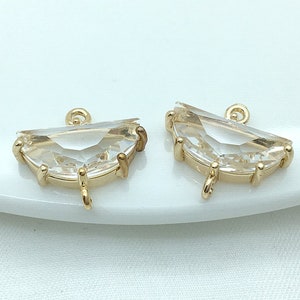 May include: Two gold-toned crystal pendant charms with a clear, faceted design. Each charm has a loop at the top for attaching to jewelry.