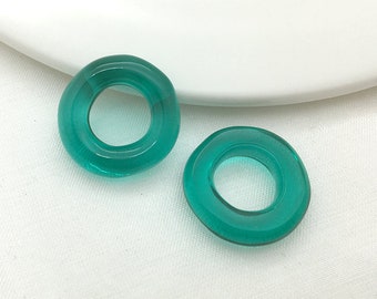 May include: Two teal green glass rings, each with a smooth, rounded surface and a hole in the center.