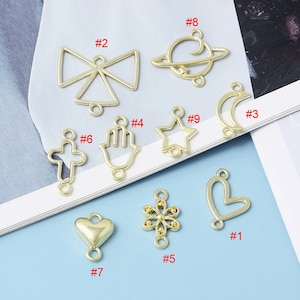 May include: Ten gold-toned metal charms with different shapes, including a bow, a star, a heart, a cross, a hand, a moon, a flower, and a planet. Each charm has two holes for attaching to jewelry or other crafts.