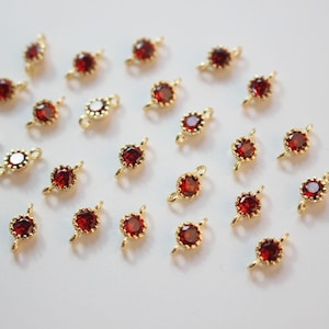 Op de afbeelding: Een verzameling van 25 goudkleurige springringen met rode kristallen accenten. Elke ring heeft aan beide zijden een kleine lus om sieraden aan te bevestigen.