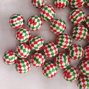 Puede incluir: Un conjunto de cuentas redondas con un patrón de cuadros rojos y verdes. Las cuentas están dispersas sobre una superficie blanca, mostrando sus colores vibrantes y diseño. Adecuado para varios proyectos de manualidades.