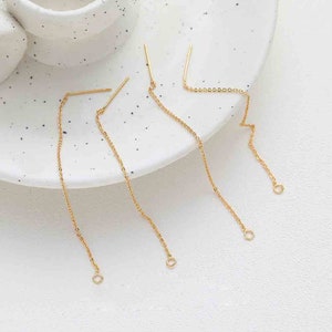 May include: Four gold chain earrings with a small bar at the top and a small loop at the bottom. The earrings are on a white surface.