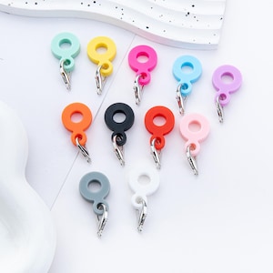Può includere: Una collezione di portachiavi circolari colorati con chiusure argentate. I portachiavi sono in vari colori, tra cui verde acqua, giallo, rosa, blu, viola, arancione, nero, rosso, rosa chiaro, grigio e bianco. Sono disposti su una superficie bianca.