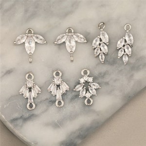 Puede incluir: Seis conectores de joyería plateados con adornos de cristal transparente. Los conectores presentan varios diseños, incluyendo formas de hoja, lágrima y geométricas.