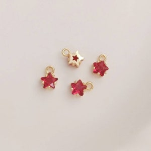 May include: Four gold star charms with red crystal centers. The charms have a loop at the top for attaching to jewelry.