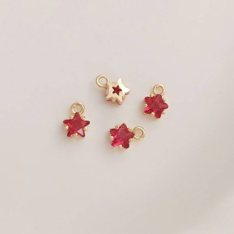 May include: Four gold star charms with red crystal centers. The charms have a loop at the top for attaching to jewelry.
