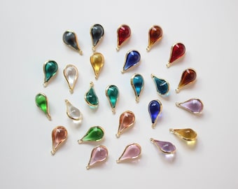 May include: Assortment of colorful glass teardrop charms with gold accents. The charms are arranged in a circle on a white background.