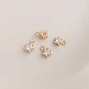 May include: Four gold star-shaped charms with clear crystal accents. The charms have a loop at the top for attaching to jewelry.