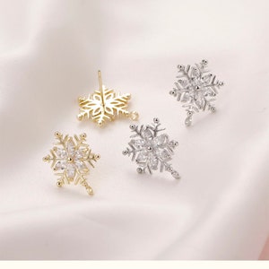 May include: Three snowflake earrings with clear rhinestones. Two earrings are gold and one is silver.