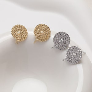 May include: Close-up of gold and silver-colored stud earrings. The earrings feature a spiral design, with a textured, rope-like appearance. The earrings are displayed on a white surface, showcasing their intricate details and metallic sheen.