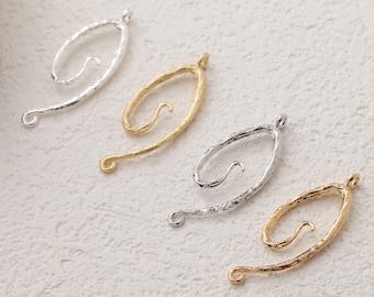 May include: Four metal pendants in silver and gold tones. Each pendant has a textured, abstract design with a loop at the top and a curved extension. The pendants are displayed on a textured, off-white surface.