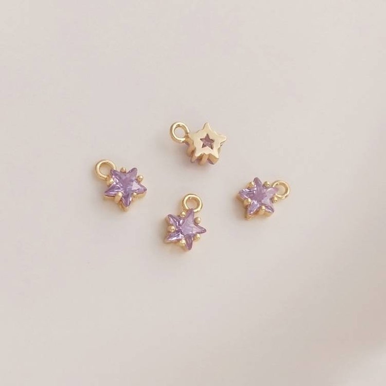 May include: Four gold star charms with a purple rhinestone center. The charms have a loop at the top for attaching to jewelry.