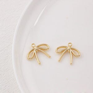May include: Two gold-coloured metal bow charms with a loop at the top for attaching to jewellery or other crafts.