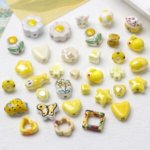Puede incluir: Surtido de cuentas de cerámica amarilla y blanca con diversas formas y diseños, incluyendo flores, estrellas, corazones, mariposas y animales. Las cuentas son perfectas para la elaboración de joyas, manualidades y decoración del hogar.