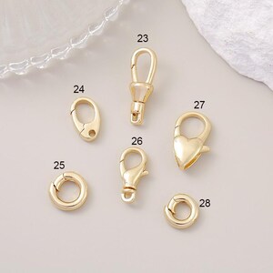 May include: Assortment of gold-toned metal clasps and jump rings. The clasps are in various shapes, including a heart, a circle, and a hook. The jump rings are round.