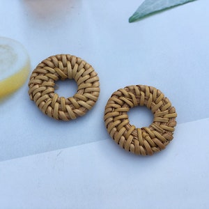 以下が含まれることがあります： 中央に穴が開いた、丸い編み込みの茶色の籐製のイヤリングが2つ