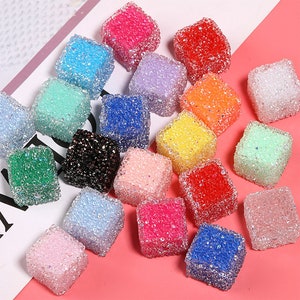 May include: Assortment of 20 colorful, glittery, square-shaped resin embellishments. Each piece has a textured, bubbly surface. The embellishments are perfect for adding a touch of sparkle to crafts, jewelry, and other projects.