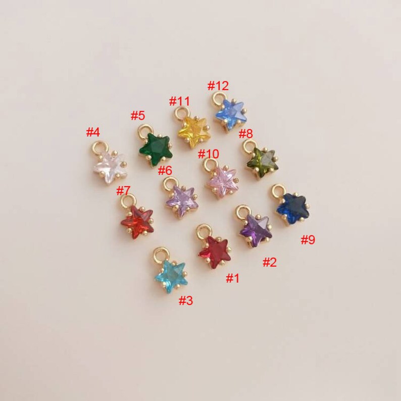 May include: Twelve gold star charms with different colored crystals. The charms are numbered 1 through 12.