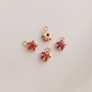 May include: Four gold star charms with red rhinestone accents. The charms have a loop at the top for attaching to jewelry.