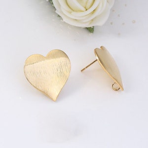 May include: A pair of gold-tone heart-shaped earring blanks with a brushed finish. The earrings have a post and a loop for attaching a charm or pendant.