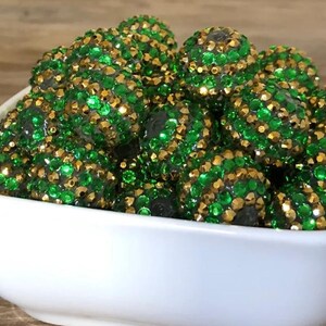 May include: A bowl filled with green and gold sparkly round beads. The beads are covered in small rhinestones.