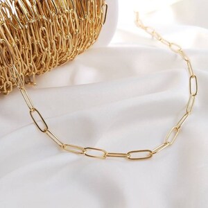 May include: A gold chain necklace with a simple, oval-shaped link design. The chain is laid out on a white surface.