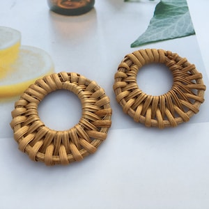 May include: Two round, woven, light brown wicker earrings. The earrings are made of natural materials and have a simple, elegant design.