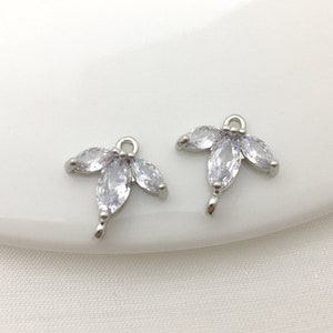 Puede incluir: Dos abalorios de metal plateado con diseño de hoja. Cada abalorio presenta cinco piedras transparentes facetadas en forma de marquesa.