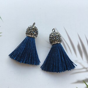 Puede incluir: Dos pendientes de borla azul oscuro con tapas plateadas adornadas con brillantes brillantes.