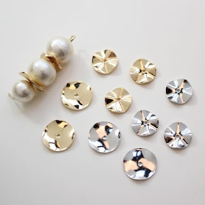 May include: A collection of gold and silver metal embellishments with a scalloped edge. The embellishments are round and have a small hole in the centre. There are also three white pearl beads with a gold connector.