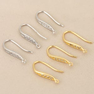 Peut inclure: Divers crochets de boucles d'oreilles argentés et dorés. Les crochets sont incurvés avec une forme décorative de goutte d'eau allongée. La partie en forme de goutte des crochets argentés est ornée de petites pierres transparentes. Les crochets dorés ont un design similaire.