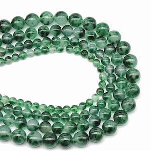 May include: A strand of green jade beads with a mottled pattern. The beads are round and smooth, and they are strung on a clear thread.
