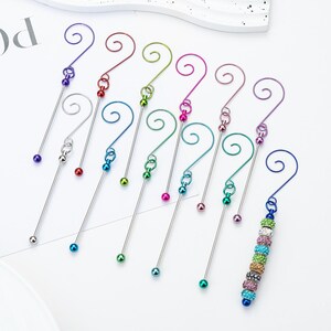 Puede incluir: Una colección de coloridos dijes para vino. Cada dije presenta un tallo delgado de color plateado con una parte superior en bucle y una cuenta decorativa en la parte inferior. Los dijes vienen en varios colores, incluyendo morado, rojo, verde, rosa y azul.