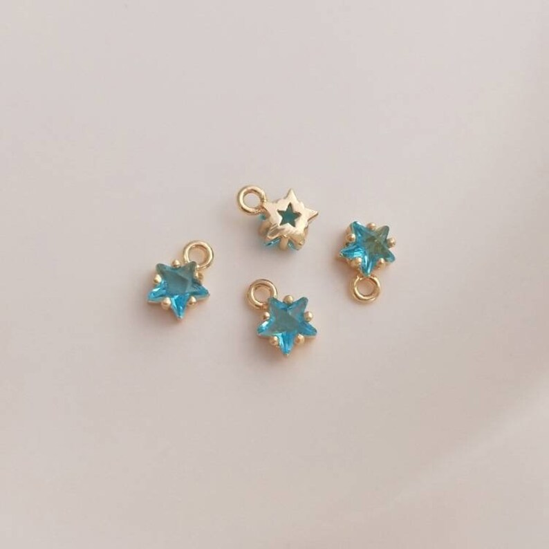 May include: Four gold star-shaped charms with blue crystal centers. The charms have a loop at the top for attaching to jewelry.