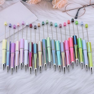 May include: A set of 20 iridescent pens with silver caps and tips. The pens are arranged in a row, with the caps facing the viewer. The pens are all different colours, including pink, blue, green, and purple.
