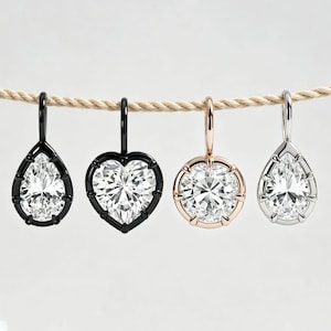 May include: Four jewellery pendants hanging from a rope. From left to right: a black pear-shaped pendant with a clear stone, a black heart-shaped pendant with a clear stone, a rose gold circular pendant with a clear stone, and a silver pear-shaped pendant.