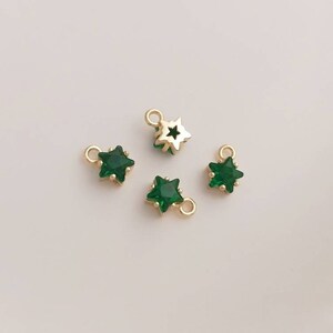 May include: Four gold star-shaped charms with green crystal centers. The charms have a loop at the top for attaching to jewelry.
