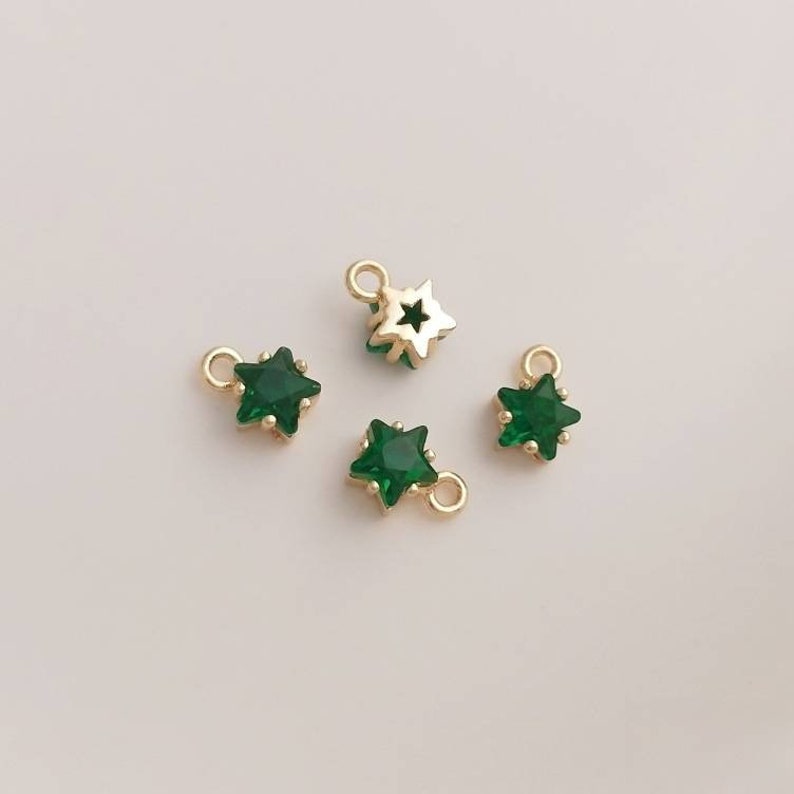 May include: Four gold star-shaped charms with green crystal centers. The charms have a loop at the top for attaching to jewelry.