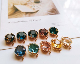 May include: Assortment of ten gold-toned metal charms with faceted glass stones in various colors, including clear, blue, green, yellow, pink, and brown. Each charm has a loop for attaching to jewelry or other crafts.